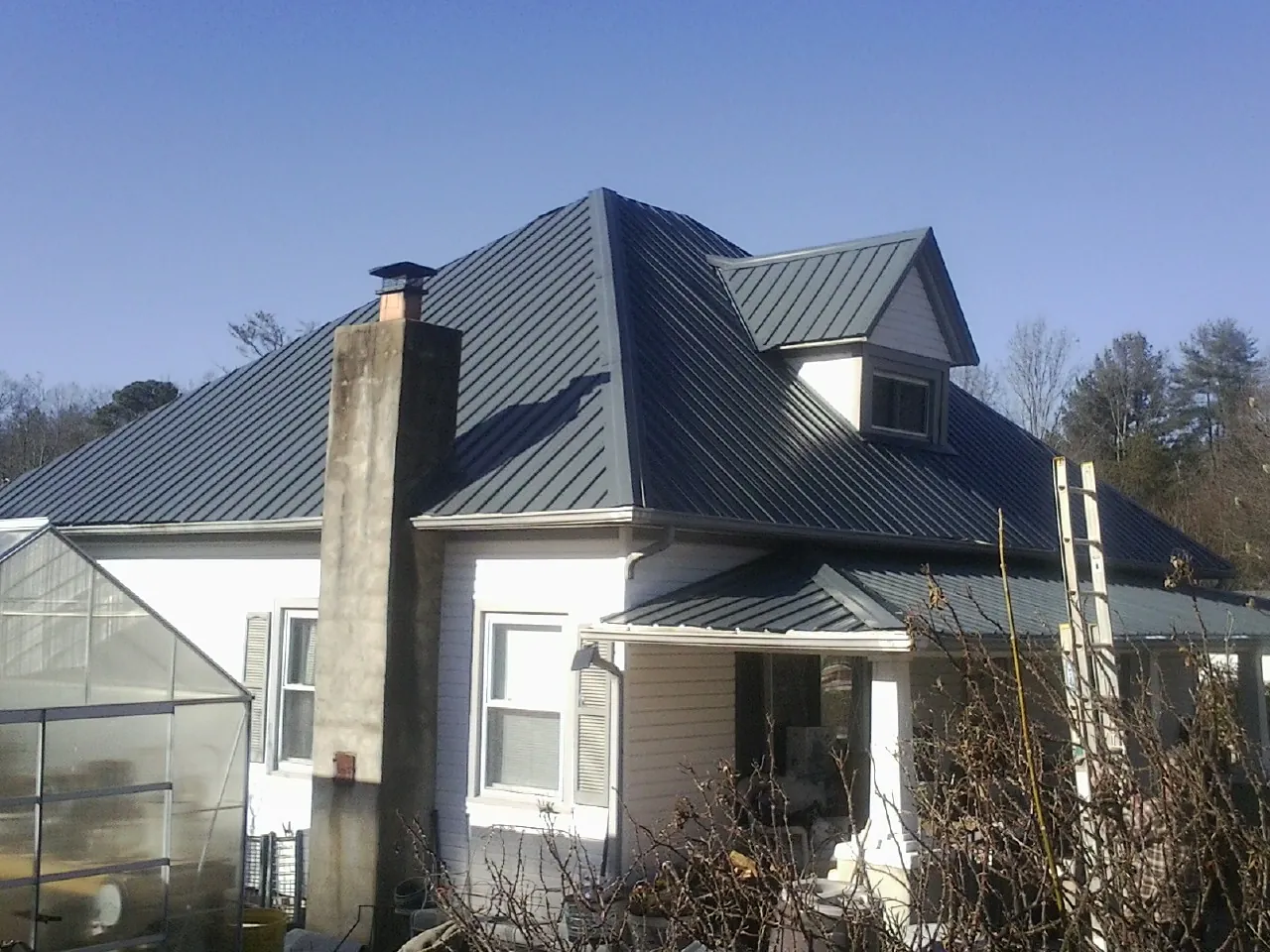 Dark blue standing seam metal roof on a white farmhouse with dormer — Slate & Tile Roof Repair by Roofing Brothers in Maxton