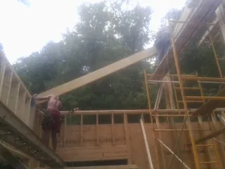 Carpenter raising a rafter beam on a new second story frame in Maxton