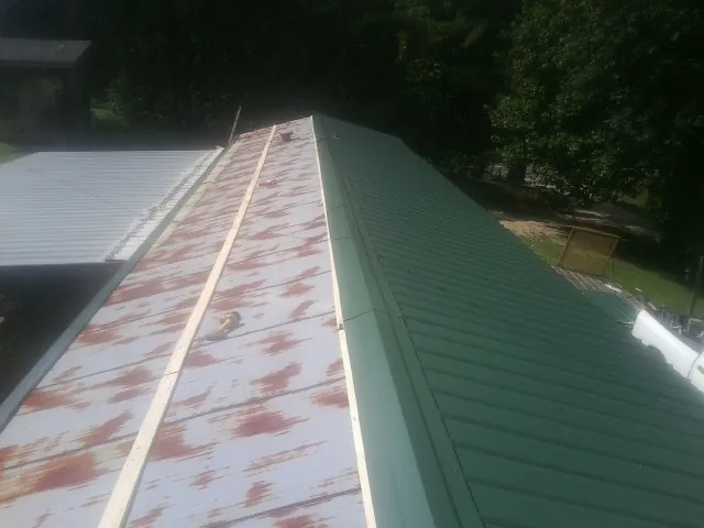 Old rusted panels beside newly installed green metal roofing — Wind Damage Roof Repair by Roofing Brothers in Maxton