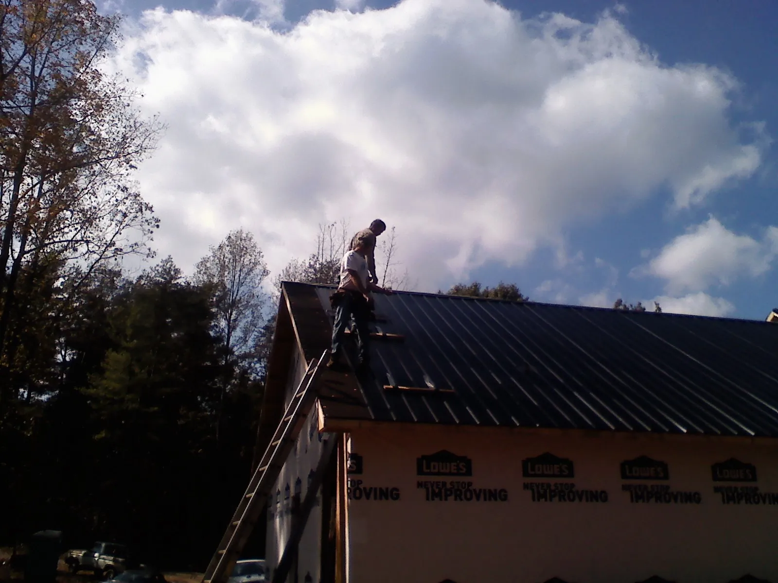 Roofer fastening dark metal panels high against a cloudy sky, from a Roof Inspection job in Maxton