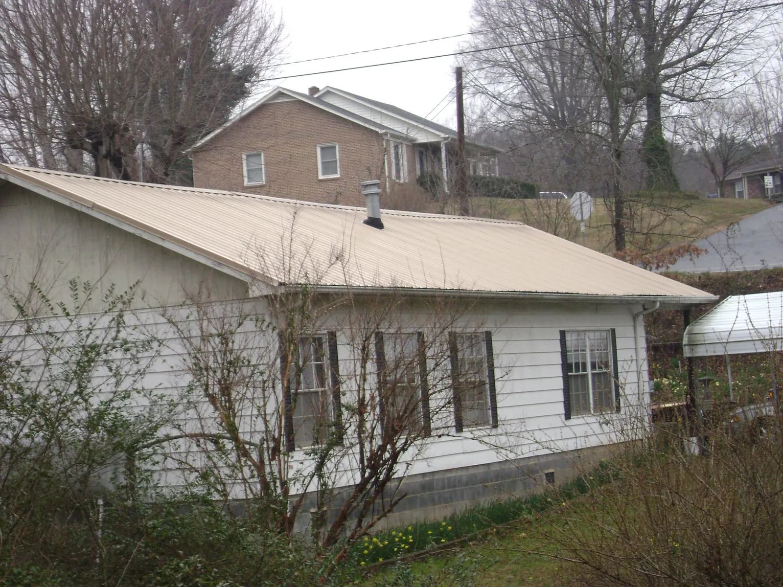 Tan metal roof on a white sided house set into a hillside — Commercial Roofing by Roofing Brothers in Maxton