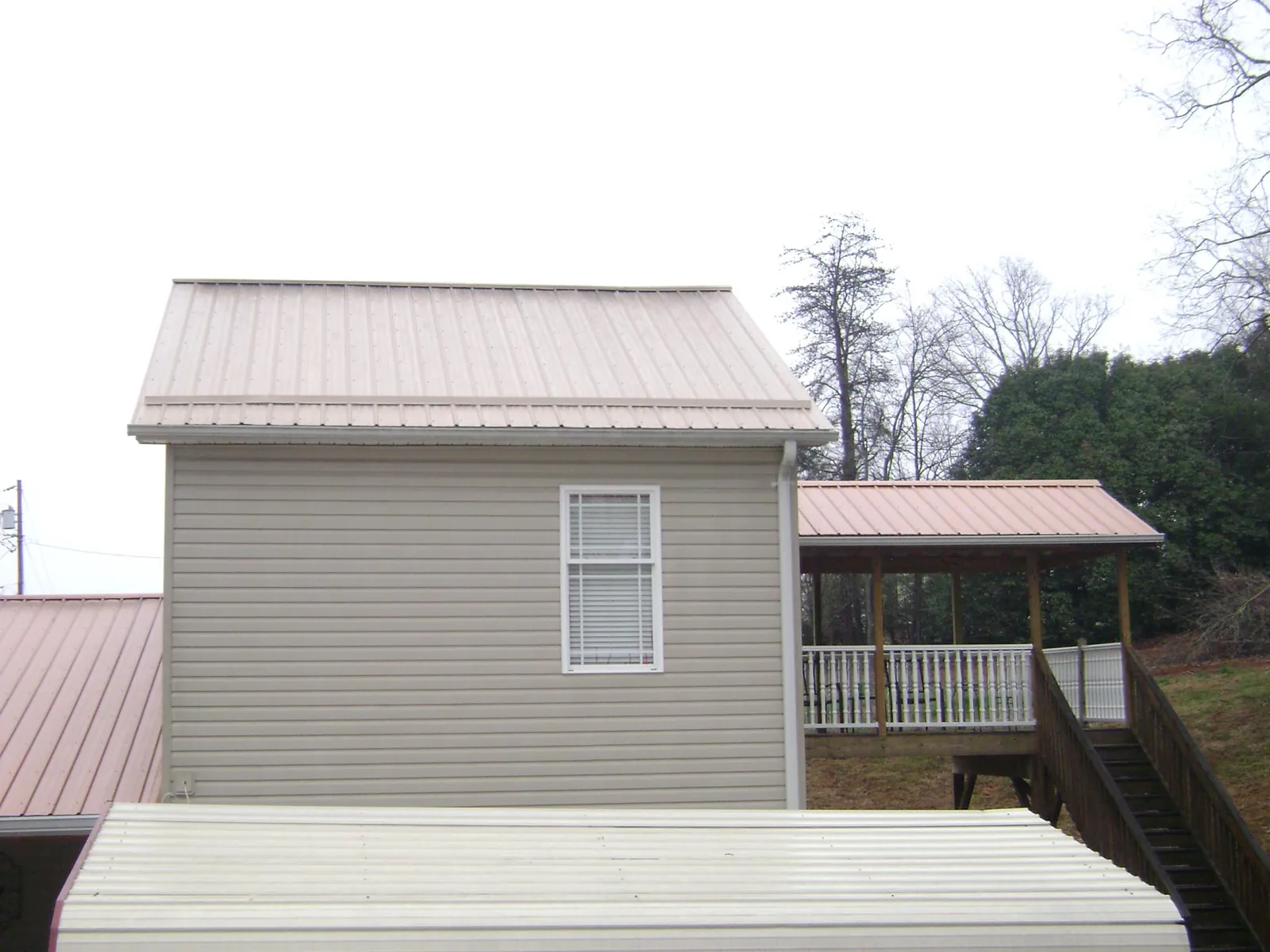 Tan metal roofs on a two story addition and attached porch, from a Roof Replacement job in Maxton